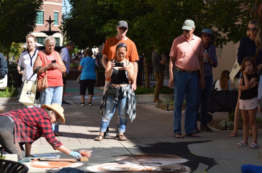 People watch and capture photos of artist Noreen Schroder as she works on her chalk art piece of a monkey during the 2023 Centennial Chalk Art Festival.